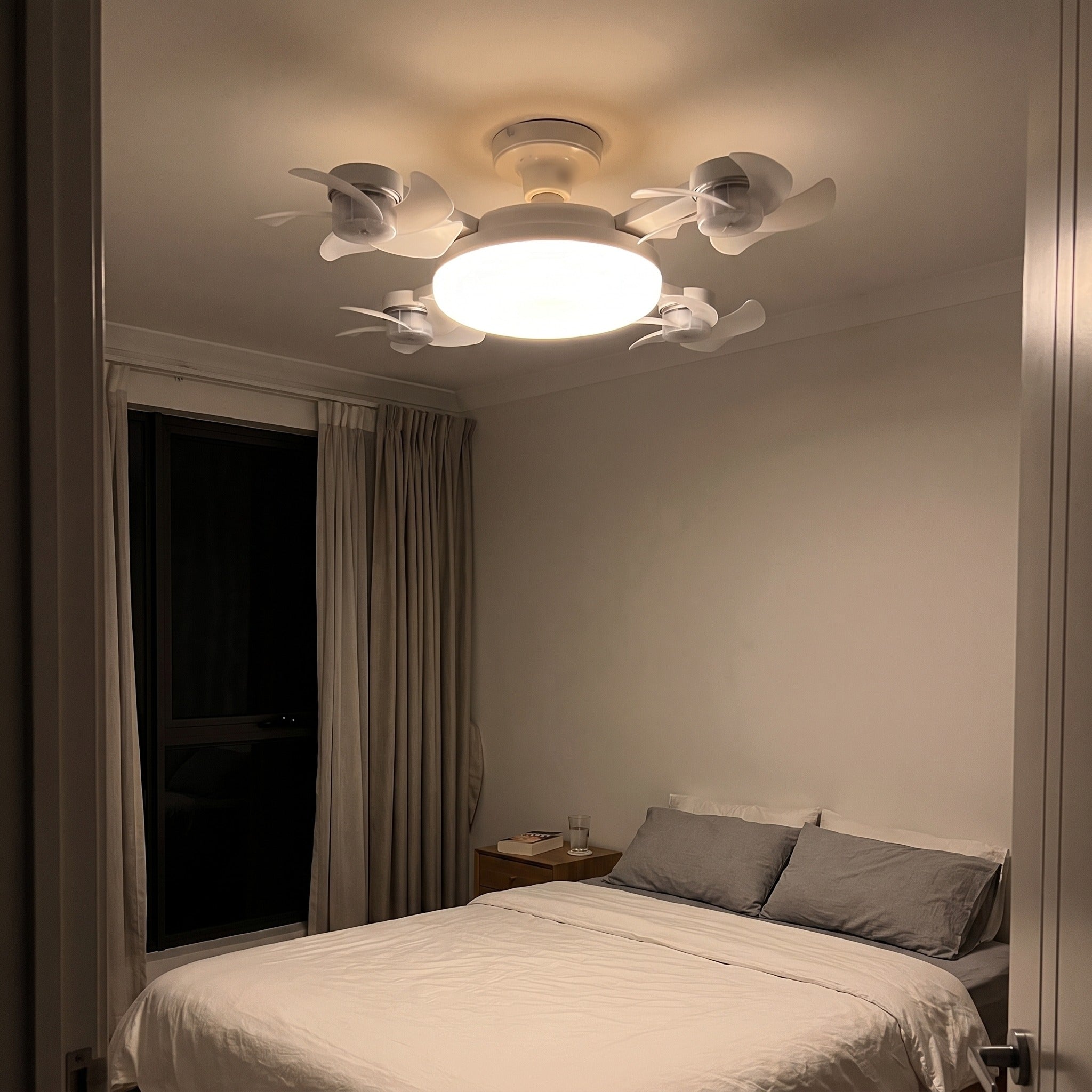 Novu Quad Fan screwed into a bedroom ceiling socket at night, glowing warm white above the bed